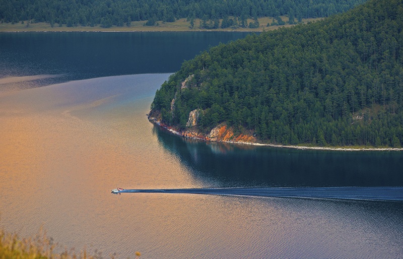Aerial view of Khovsgol Lake with forested shoreline and boat in Mongolia